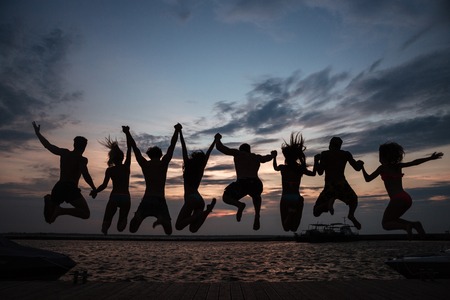 Rear view of friends jumping into water during summer vacation in front of a sunsetの写真素材