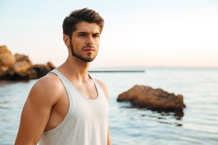 Young handsome man athlete standing at the rocky beach by the seaの写真素材