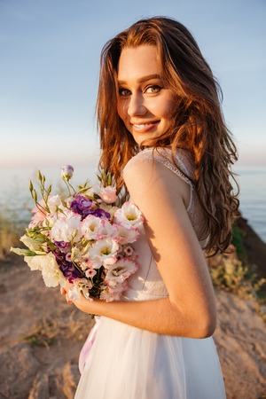 Portrait of beautiful bride standing by the beach holding fowers bouquetの写真素材