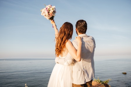 Back view of a romantic happy married couple standing at the beachの写真素材