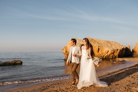 Just-married couple walking at the beach at sunset