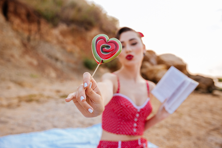 Happy young cheerful pin up girl showing heart shaped candy at the beachの写真素材