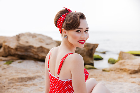 Close up portrait of a happy cheerful pin up girl in red swimsuit sitting on the beachの写真素材