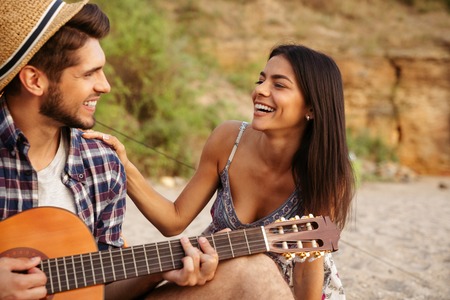 Portrait of a man playing guitar for his girlfriend sitting at the camping tent