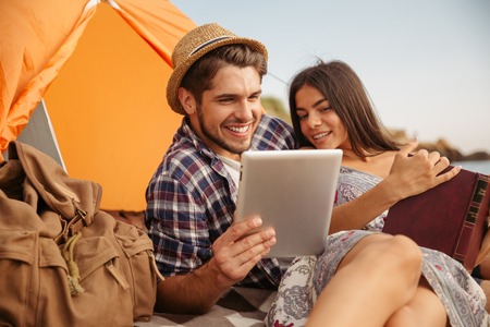 Portrait of a happy couple sitting at the tent using tablet computer and reading bookの写真素材
