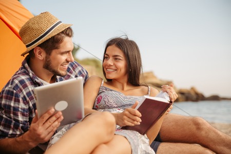 Portrait of a happy couple sitting at the tent using tablet computer and reading bookの写真素材