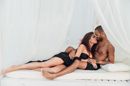 Beautiful young couple lying and kissing on white bedの写真素材