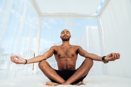 Handsome young african man in shorts sitting and meditating on the beach bedの写真素材