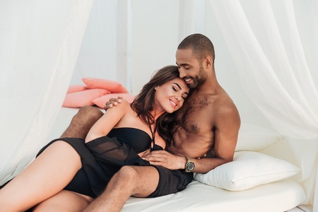 Happy young couple lying and hugging on white bedの写真素材