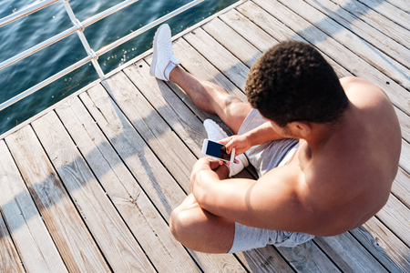 Top view of afro american sports man resting after workout and listen music at the wooden pierの写真素材