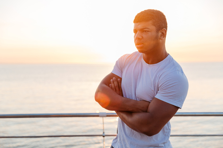 Pensive african american young man standing with arms crossed on sunriseの写真素材