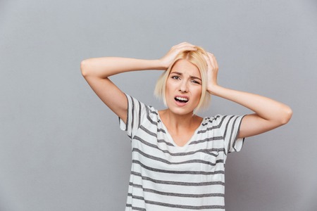 Upset stressed young woman having a headache over gray backgroundの写真素材