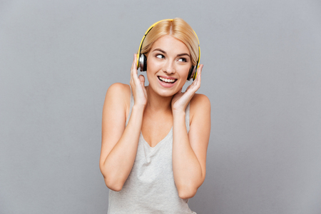 Happy beautiful young woman in headphones listening to music over gray backgroundの写真素材