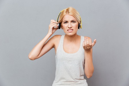Frowning irritated young woman taking off headphones over gray backgroundの写真素材