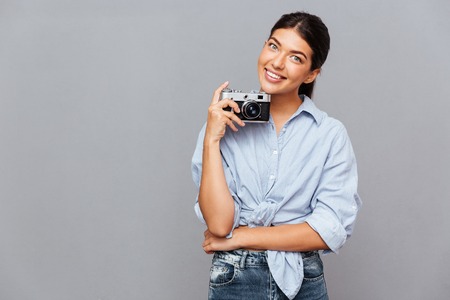 Smiling young brunette girl holding photo camera isolated on a gray backgroundの写真素材