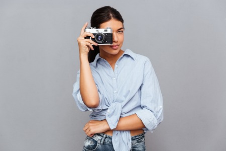 Cheerful young brunette woman making photo with camera isolated on a gray backgroundの写真素材