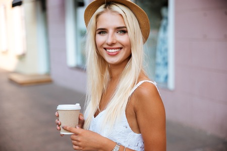 Close up portrait of a smiling young girl in hat holding take away coffee cup outdoorsの写真素材