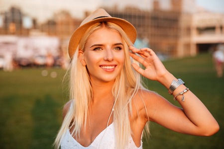 Close up portrait of a young smiling blonde woman listening music with earphones and smartphone at the parkの写真素材