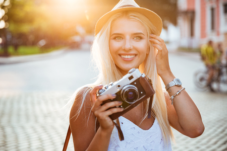 Close up portrait of a smiling young blonde girl holding retro camera outdoorsの写真素材