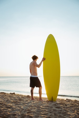 Man with his surfboard standing on the beach and looking at the horizonの写真素材
