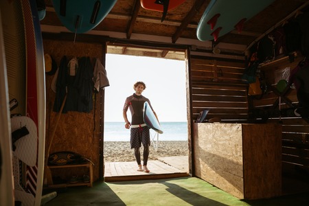 Young surfer guy carrying surf board to the surf shack at the beachの写真素材