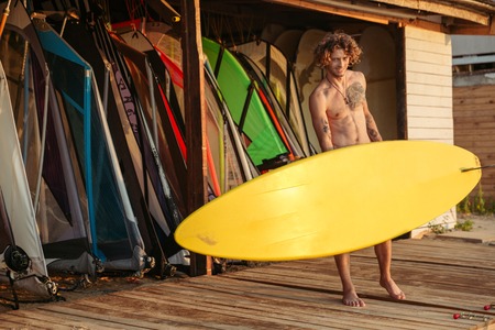 Young smiling professional surfer holding surf board at the shackの写真素材