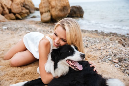 Happy pretty young woman relaxing and hugging her dog on the beachの写真素材