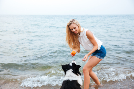 Happy pretty young woman playing with dog using ball on the beachの写真素材