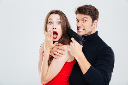 Mad criminal young man threatening to scared young woman with gunの写真素材