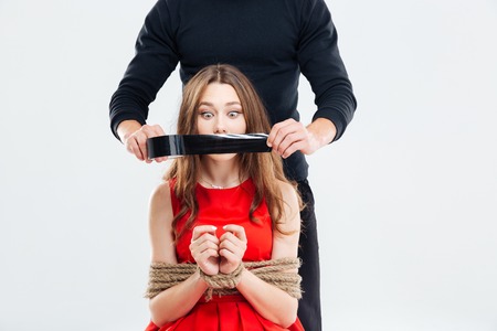 Criminal man covering mouth of woman bounded with ropes by black tapeの写真素材