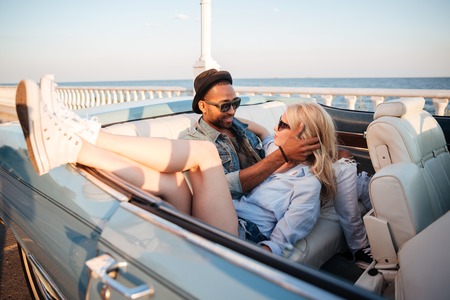 Multiethnic happy young couple sitting and hugging in cabriotetの写真素材