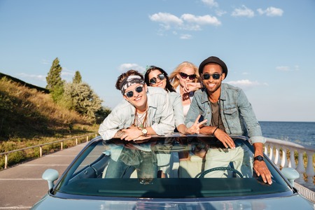 Group of cheerful young friends driving car in summerの写真素材