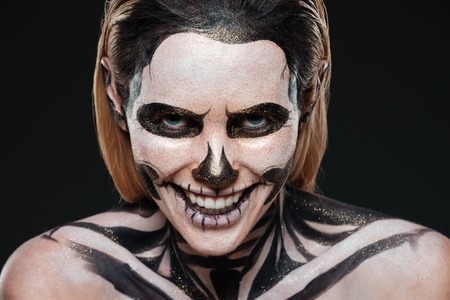 Smiling young woman with skeleton halloween makeup laughing over black backgroundの写真素材