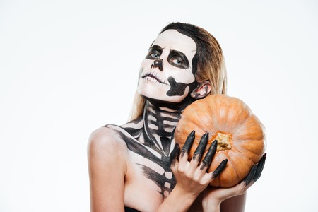 Portrait of woman with halloween skeleton makeup holding pumpkin over white backgroundの写真素材