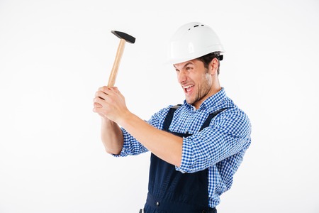 Funny young builder applying hummer to his head in helmet and having fun isolated on a white backgroundの写真素材