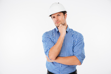 Pensive young man builder in hard hat standng and thinkingの写真素材