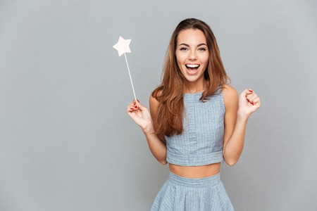 Happy amazed young woman holding magic wand over grey backgroundの写真素材
