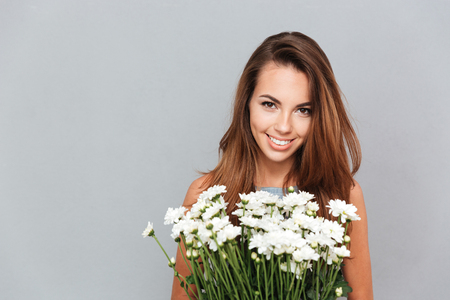 Closeup of cheerful attractive young woman with bunch of flowers over grey backgroundの写真素材