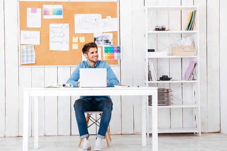 Full length portrait of a happy young handsome businessman using laptop computer in office