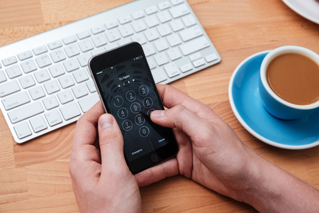 Hands holding smartphone with access identification password on the screen over wooden tableの写真素材