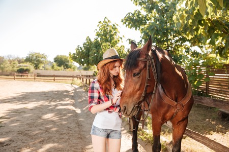 Cute young woman cowgirl taking care and hugging her horse at ranchの写真素材