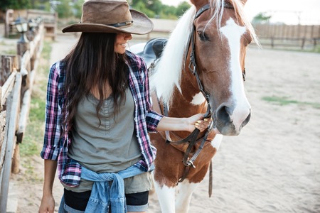 Smilng lovely young woman cowgirl with her horse in villageの写真素材