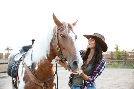 Happy beautiful young woman cowgirl taking care of her horseの写真素材