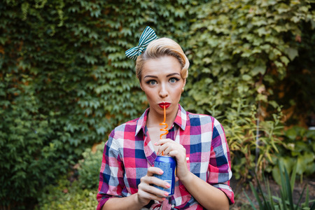 Cute playful pin-up girl drinking soda in the garden in summerの写真素材