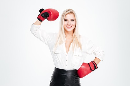 Happy young businesswoman in boxing gloves showing biceps over white backgroundの写真素材