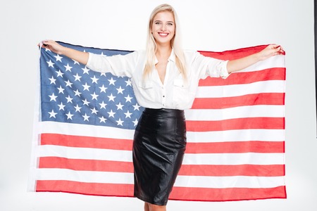 Cheerful young businesswoman holding flag of United states over white backgroundの写真素材