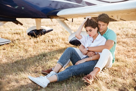 Sensual young couple sitting and embracing near private aircraftの写真素材