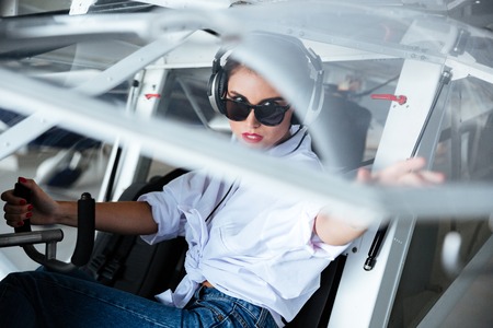 Serious young woman pilot in headset sitting in small planeの写真素材