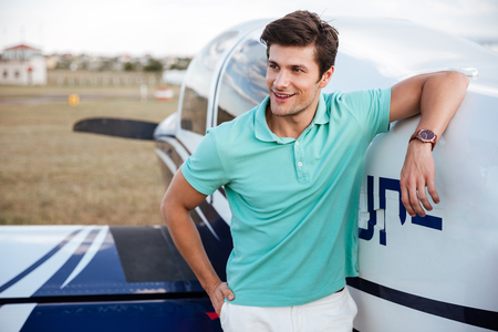 Happy handsome young man standing in field near small private airplaneの写真素材