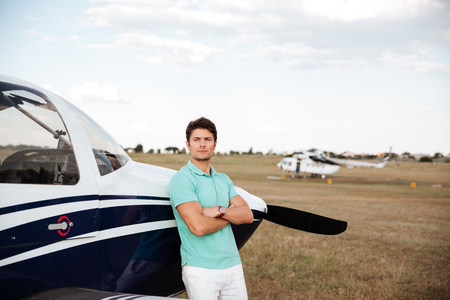 Serious handsome young man standing with arms crossed near small planeの写真素材